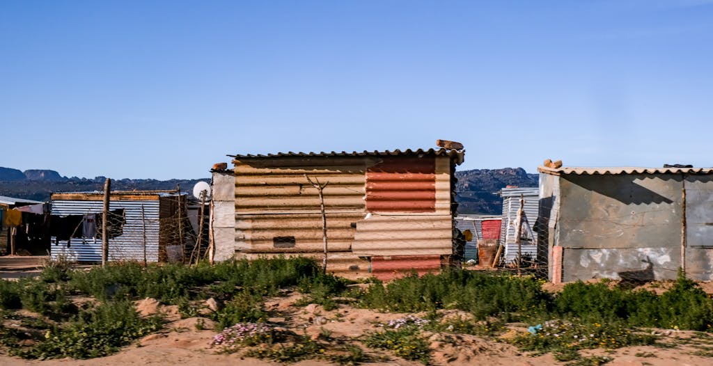 A rural community featuring rustic metal huts surrounded by natural landscapes under a clear sky.