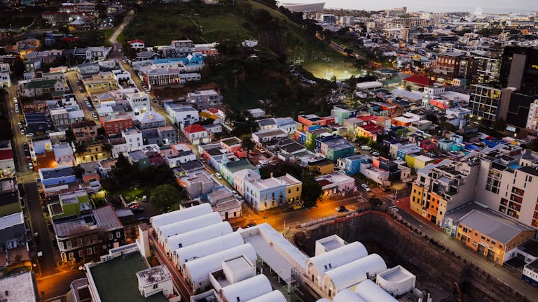 Stunning aerial view of Bo-Kaap, Cape Town with colorful houses illuminated at dusk, showcasing urban landscape.