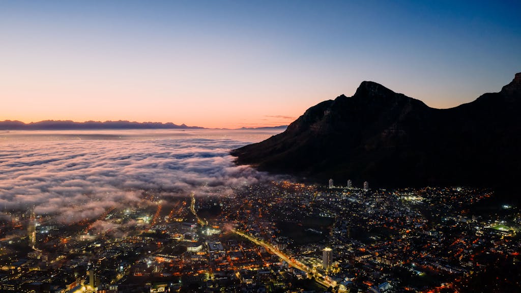 Stunning aerial view of Cape Town with cloud cover and mountains at twilight, showcasing vibrant city lights a digital nomad favourite